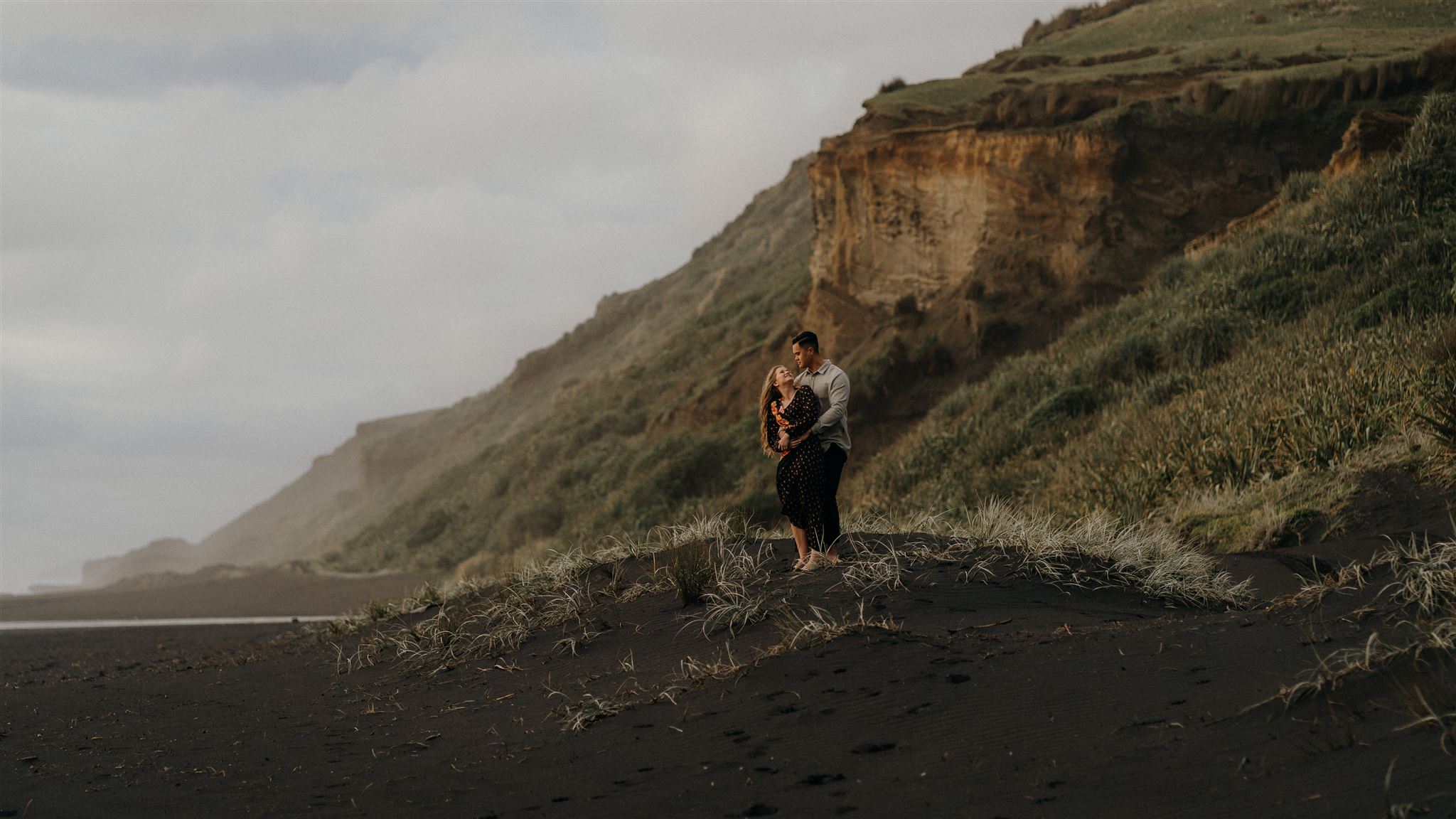 A newly engaged couple stand on a sand du