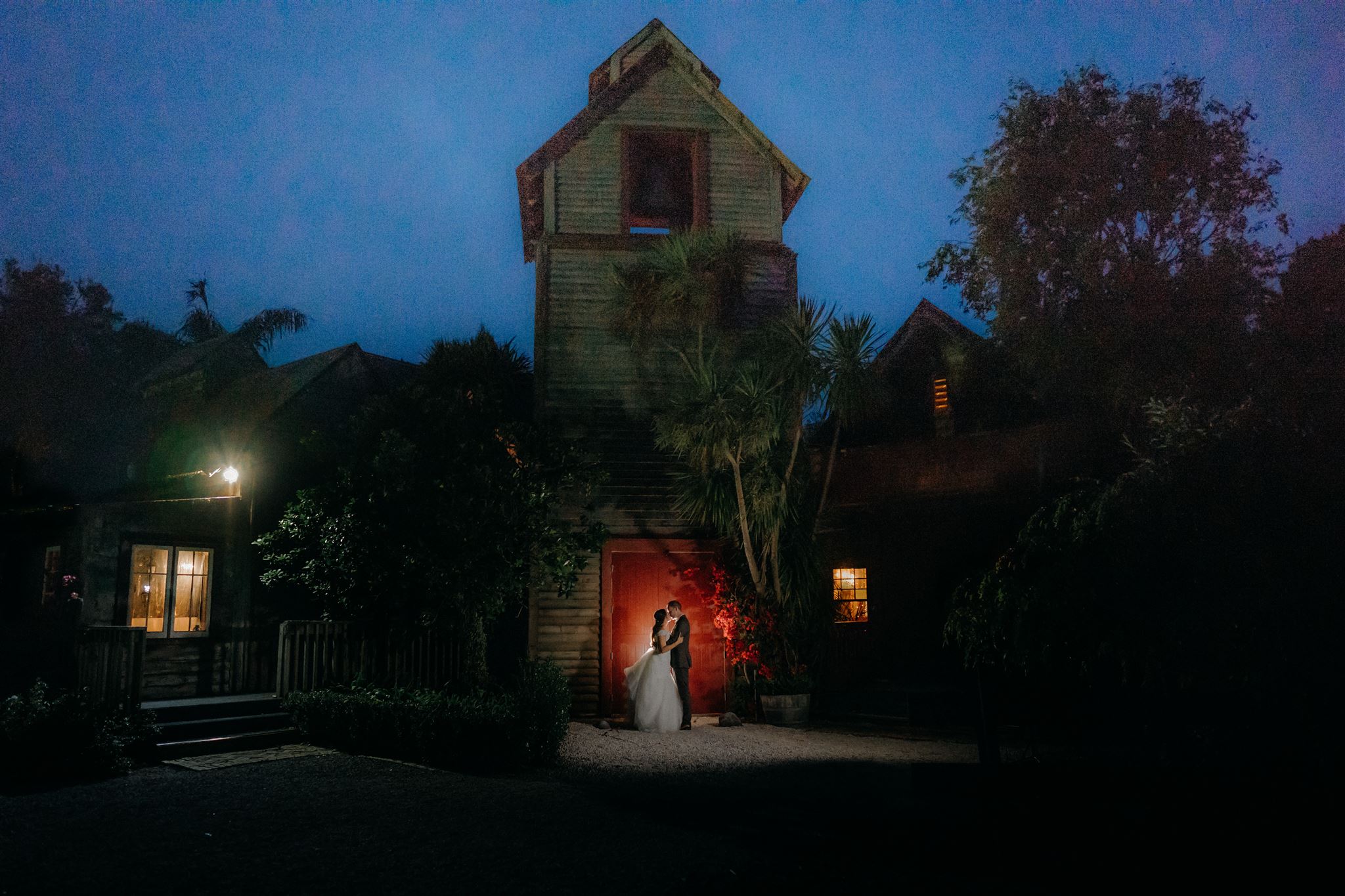 A couple stand silhouetted outside the red door of Kumeu valley estate on their wedding day for a photo