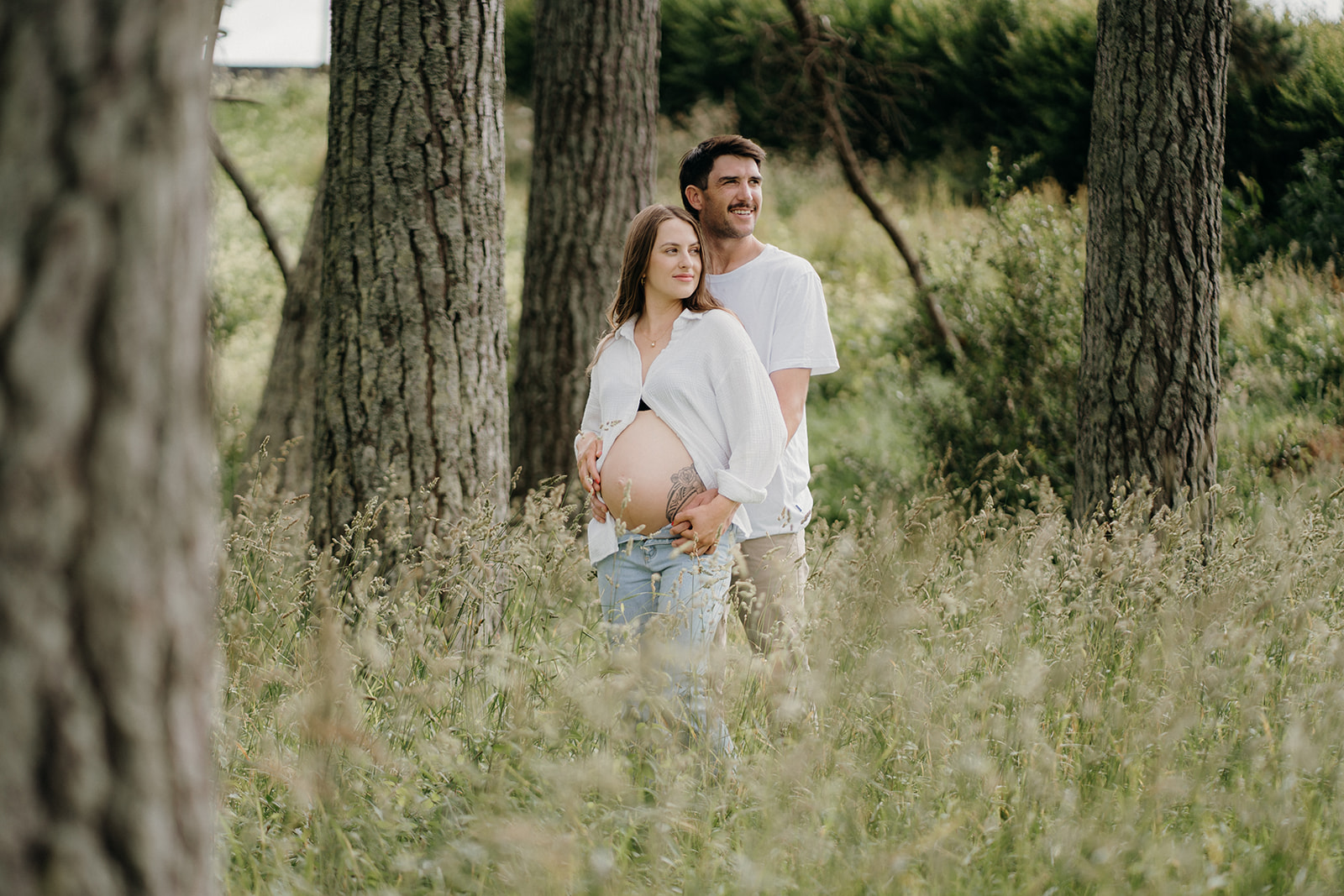 A couple stand in a field embracing during their maternity shoot.